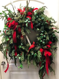 a wreath with red bows and greenery hanging on the front door to welcome guests