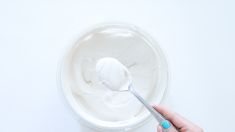 a hand holding a spoon over a bowl of yogurt on a white surface