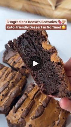 a person holding a piece of chocolate cake in front of some brownies on a plate