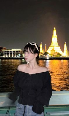 a woman standing in front of a body of water at night with buildings in the background