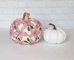 two painted pumpkins sitting next to each other on a white counter top with brick wall in the background