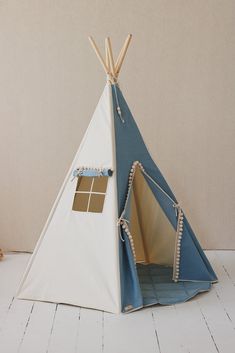 a teepee tent sitting on top of a white floor next to a window with blue trim