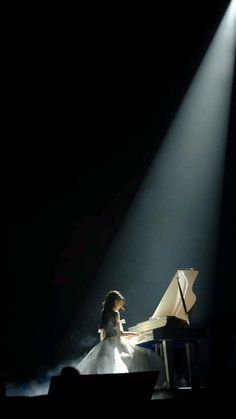 a woman sitting at a piano in front of a microphone on stage with light coming from behind her