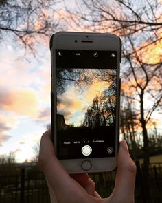 someone holding up their cell phone to take a photo with the sky in the background