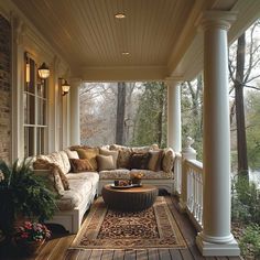 a porch with couches and rugs on the wooden flooring next to trees