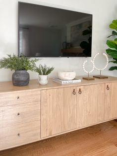 a flat screen tv mounted on top of a wooden cabinet next to a potted plant