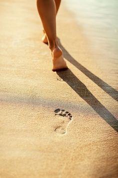 a woman walking on the beach with her footprints in the sand