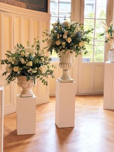 two vases with flowers are on pedestals in a room