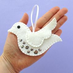 a hand holding a white bird ornament with beads on it's wings