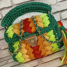 a green, yellow and red purse sitting on top of a wooden table next to a brick wall