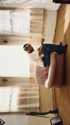 a man sitting on top of a couch in a living room next to a window