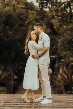 an engaged couple kissing in front of trees