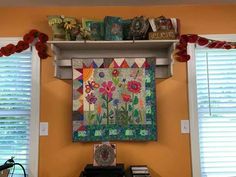 a wall hanging on the side of a yellow room with books and decorations above it