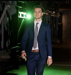 a man in a suit and tie walks down the runway at night with green lights behind him