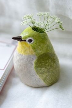 a small green and yellow bird sitting on top of a white table cloth next to a book