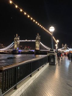 people are walking on the bridge over the river thames at night with lights strung above them