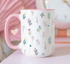 a pink and white coffee mug with flowers on it sitting on a table next to a clock