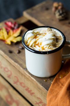 a white cup filled with whipped cream on top of a wooden table next to autumn leaves