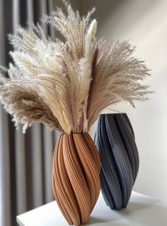 two vases with dried plants in them on a table