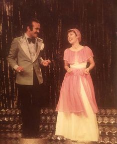 a man and woman standing next to each other in front of a wall with beads