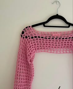 a pink crocheted sweater hanging on a hanger