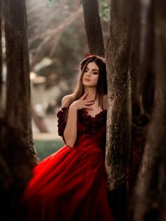 a woman in a red dress is leaning against a tree