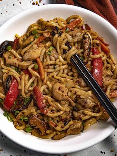 a white bowl filled with noodles and vegetables next to chopsticks on a table