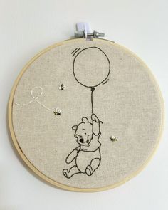 the embroidery is hanging on the wall and it has a teddy bear holding a balloon