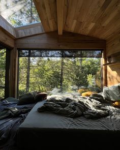 an unmade bed sitting under a window next to a forest