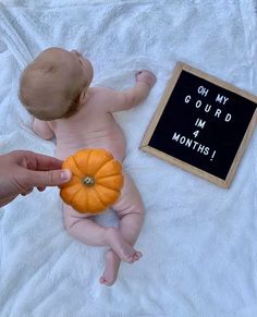 a baby laying on its back next to a sign that says oh my gourd in 4 months