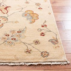 a beige rug with flowers and leaves on the top is laying on a wooden floor