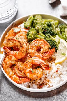 a bowl filled with shrimp, rice and broccoli next to a glass of water