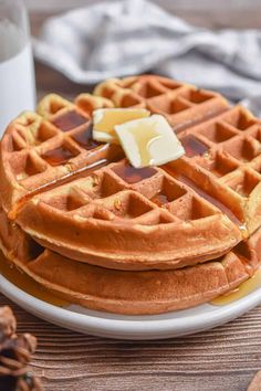 a white plate topped with waffles covered in syrup and butter next to a glass of milk