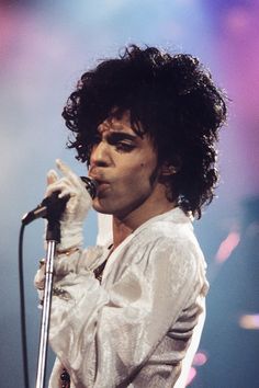 a man with curly hair on stage holding a microphone and singing into the microphone while wearing a white shirt