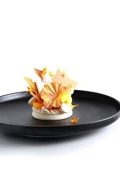 a black plate topped with an orange and yellow flower arrangement on it's side