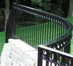 a curved metal fence next to a brick wall and green grass in the back ground