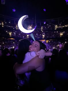 two people hugging each other in front of an audience at a concert with the moon and stars above them