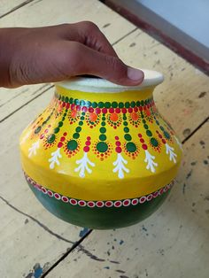 a hand that is holding onto a yellow and green vase with designs on the side