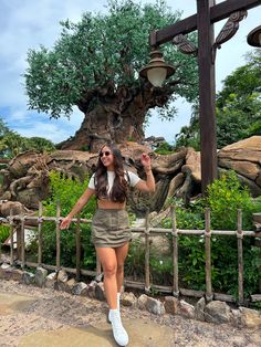 a woman is posing in front of an animal park tree with her hand on her hip