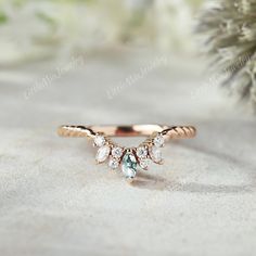 a gold ring with three pear shaped diamonds on it, sitting next to a pine tree