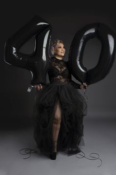 a woman in a black dress holding up the number 40 balloon with her legs and hands