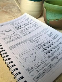 a notebook with some drawings on it next to two coffee mugs and a potted plant