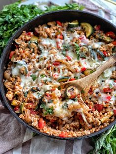 a skillet filled with pasta and vegetables on top of a table next to a wooden spoon