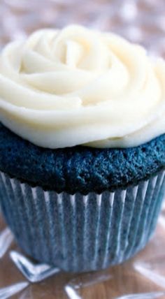 a blue cupcake with white frosting sitting on top of a glass tablecloth