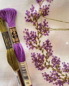 two skeins of yarn and some flowers on a white tablecloth with purple thread