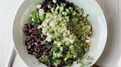 a white bowl filled with black beans, cucumbers and dill sprouts