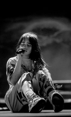 a woman sitting on the ground while holding a microphone in her hand and looking up