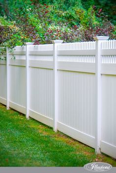 a white vinyl fence with grass and bushes in the back ground, along side it