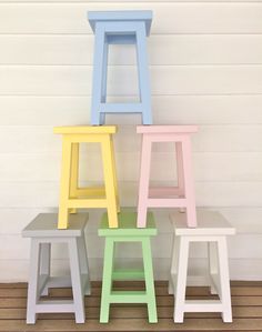 four different colored stools sitting next to each other on a wooden floor in front of a white wall