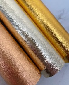 three gold and silver foil rolls on top of each other, one is white and the other is pink